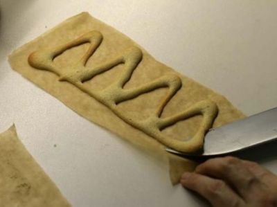 Достаньте одну бумажку с фигуркой из духовки. Ножом быстро снимаем выпеченное с бумаги и сворачиваем.