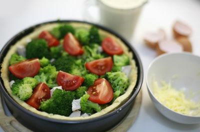 Выложите на готовый корж половину сыра, курицу, капусту, брокколи, помидоры.